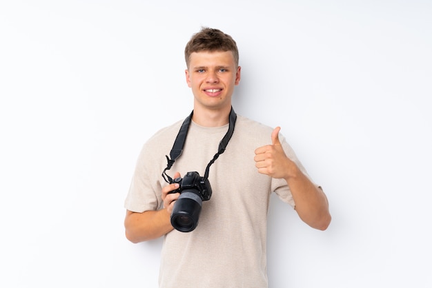 Jeune bel homme sur blanc isolé avec une caméra professionnelle et avec le pouce vers le haut