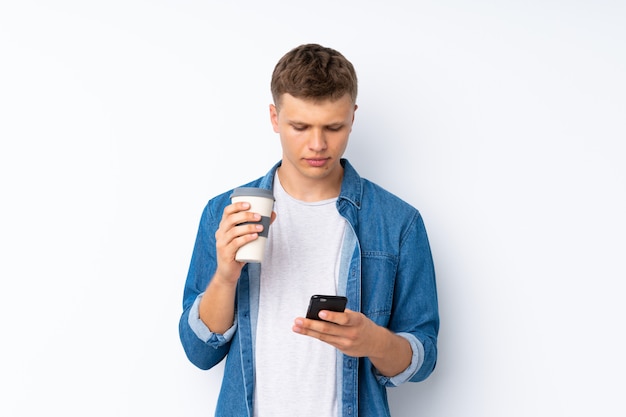 Jeune bel homme sur blanc isolé tenant un café à emporter et un mobile