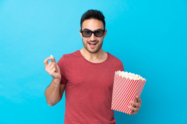 Jeune bel homme sur bleu avec des lunettes 3d et tenant un grand seau de pop-corn