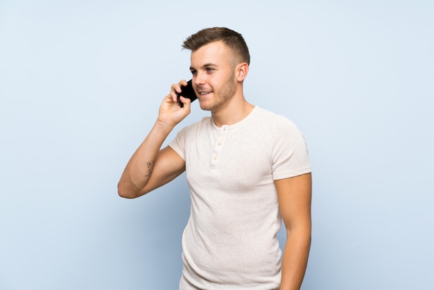 Jeune bel homme blond sur bleu isolé à l'aide de téléphone portable