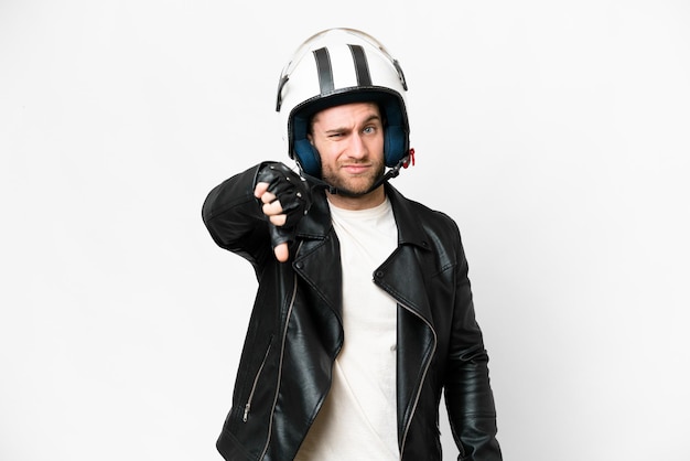 Jeune bel homme blond avec un casque de moto sur fond blanc isolé montrant le pouce vers le bas avec une expression négative