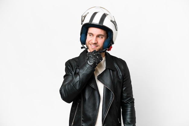 Jeune bel homme blond avec un casque de moto sur fond blanc isolé regardant sur le côté et souriant