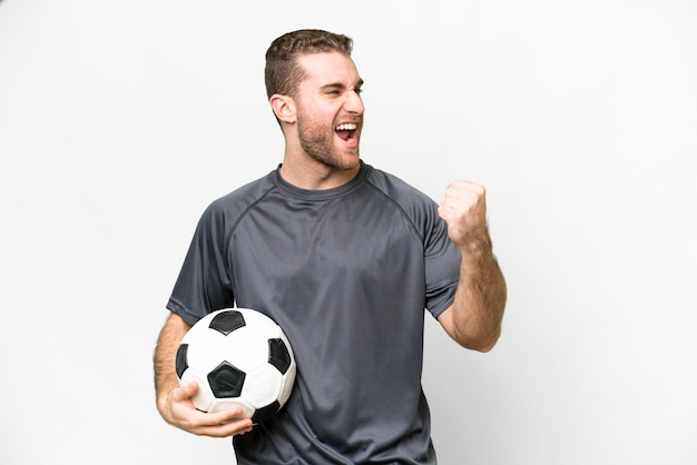 Jeune bel homme blond sur fond blanc isolé avec ballon de football célébrant une victoire