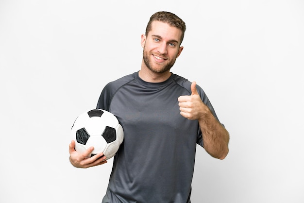 Jeune bel homme blond sur fond blanc isolé avec ballon de football et avec le pouce vers le haut