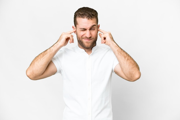 Jeune bel homme blond sur fond blanc isolé frustré et couvrant les oreilles