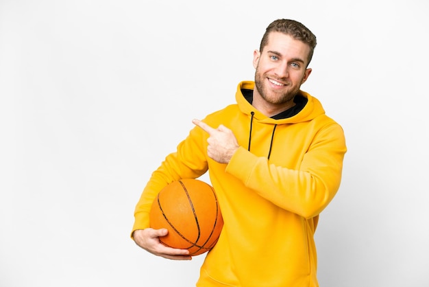 Jeune bel homme blond sur fond blanc isolé jouant au basket-ball et pointant vers le latéral