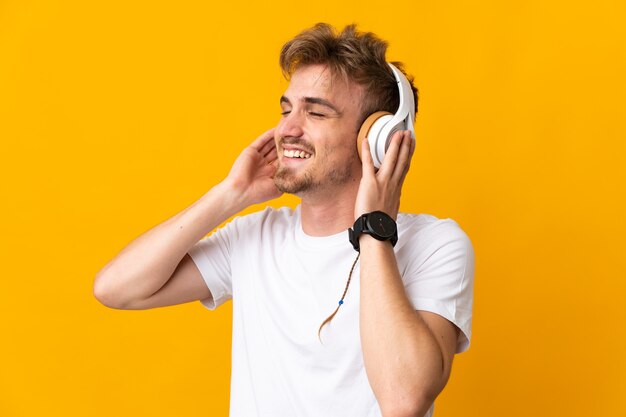 Jeune bel homme blond isolé sur fond jaune écoute de la musique et du chant