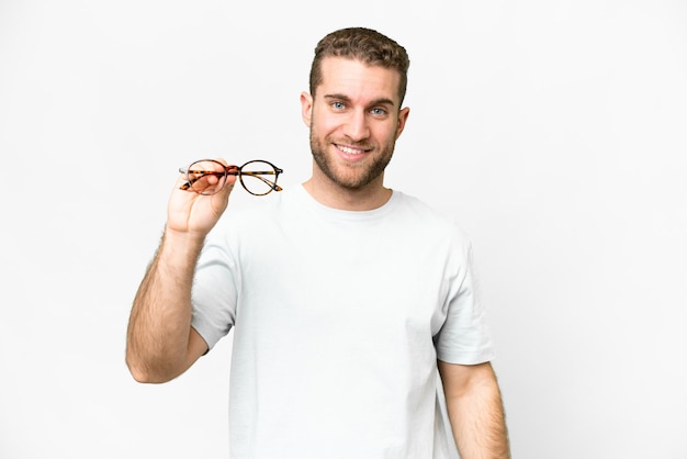 Jeune bel homme blond avec des lunettes sur fond blanc isolé avec une expression heureuse