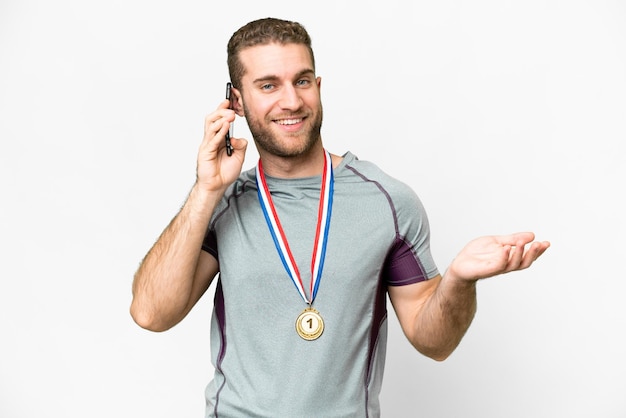 Jeune bel homme blond avec des médailles sur fond blanc isolé en gardant une conversation avec le téléphone portable avec quelqu'un