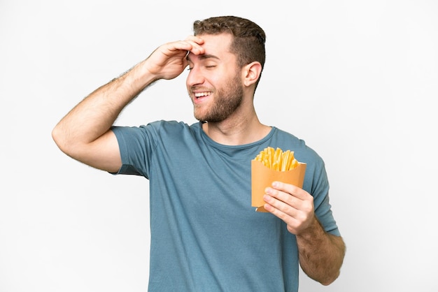 Jeune bel homme blond tenant des frites frites sur fond blanc isolé souriant beaucoup