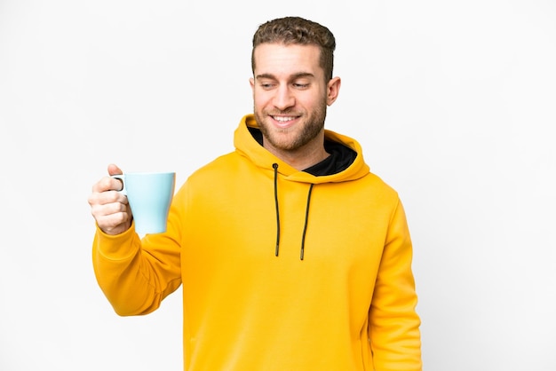 Jeune bel homme blond tenant une tasse de café sur fond isolé avec une expression heureuse