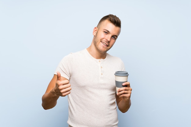 Jeune bel homme blonde sur mur bleu isolé, tenant une tasse de café