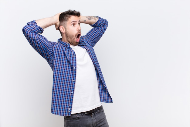 Jeune bel homme avec la bouche ouverte, l'air horrifié et choqué à cause d'une terrible erreur, levant les mains pour se diriger contre le mur de couleur plat