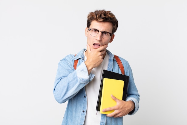 Jeune bel homme avec la bouche et les yeux grands ouverts et la main sur le menton. concept d'étudiant universitaire