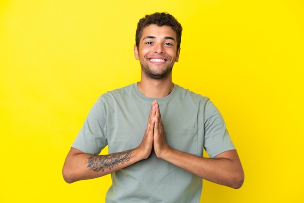 Jeune bel homme brésilien isolé sur fond jaune garde la paume ensemble La personne demande quelque chose