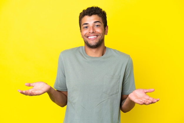 Jeune bel homme brésilien isolé sur fond jaune heureux et souriant