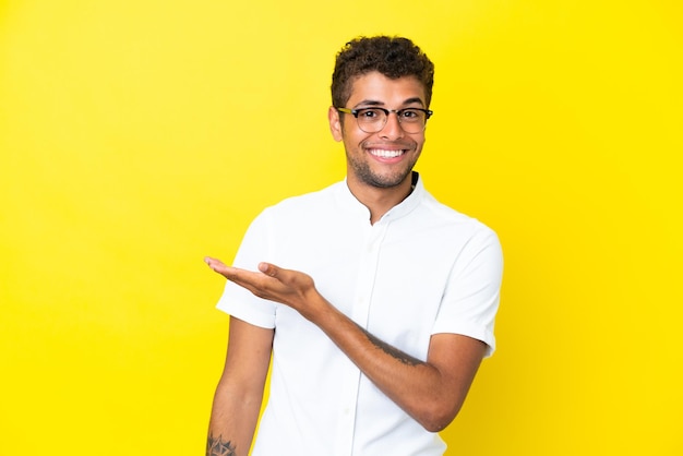 Jeune bel homme brésilien isolé sur fond jaune présentant une idée tout en regardant en souriant vers