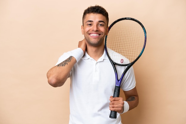 Jeune bel homme brésilien jouant au tennis isolé sur fond beige en riant