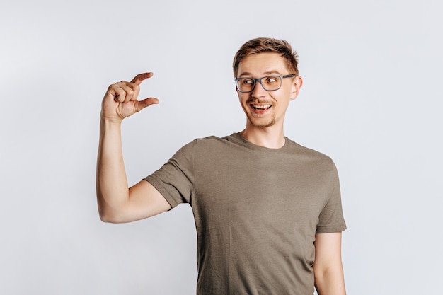 Jeune bel homme brune avec barbe portant des lunettes montre les doigts de petite taille et sourit sur fond blanc isolé