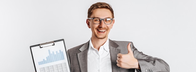 Jeune bel homme brune à lunettes sourit et montre les pouces vers le haut avec des documents sur fond gris isolé