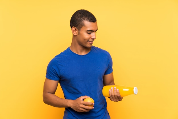 Jeune bel homme brune sur un mur jaune tenant une orange