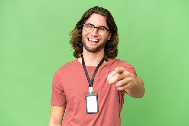 Jeune bel homme avec carte d'identité sur fond isolé pointant vers l'avant avec une expression heureuse