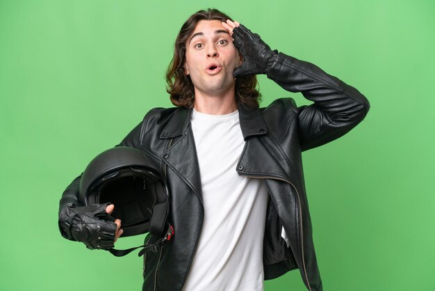 Photo jeune bel homme avec un casque de moto isolé sur fond vert chroma avec une expression surprise