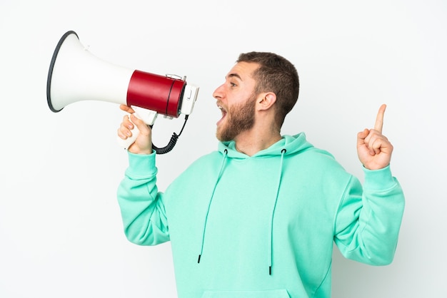 Jeune bel homme caucasien isolé sur blanc criant à travers un mégaphone pour annoncer quelque chose en position latérale