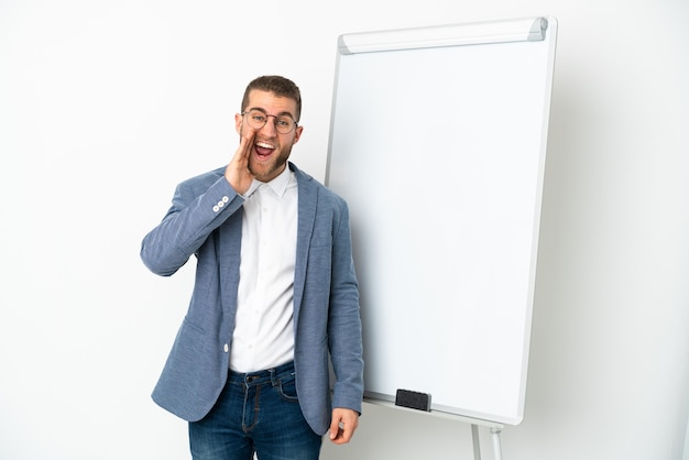 Jeune bel homme caucasien isolé sur fond blanc donnant une présentation sur tableau blanc et criant avec la bouche grande ouverte