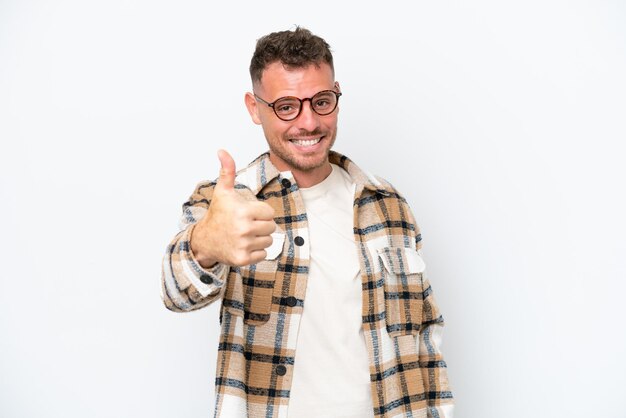 Jeune bel homme caucasien isolé sur fond blanc avec les pouces vers le haut parce que quelque chose de bien s'est produit