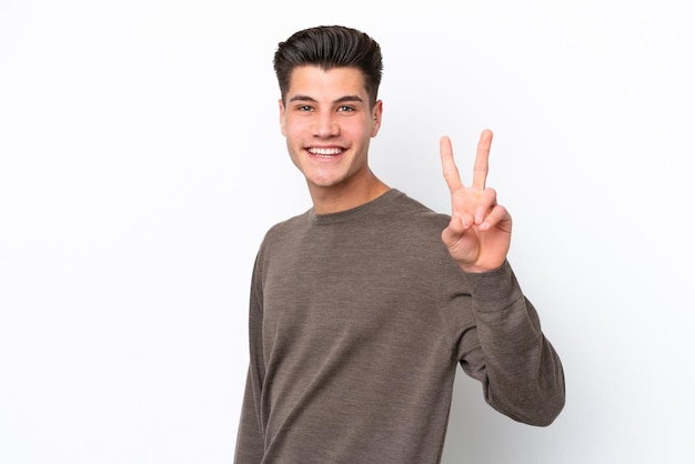 Jeune bel homme caucasien isolé sur fond blanc souriant et montrant le signe de la victoire