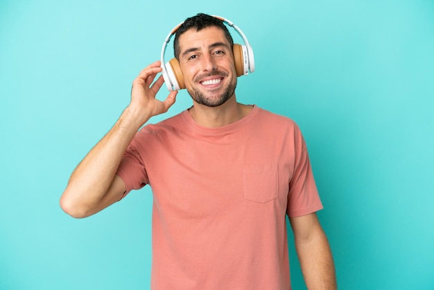 Jeune bel homme caucasien isolé sur fond bleu écoutant de la musique