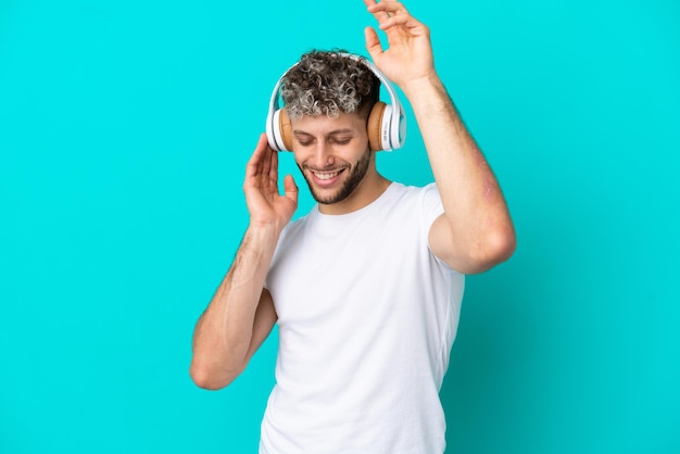 Jeune bel homme caucasien isolé sur fond bleu, écouter de la musique et danser