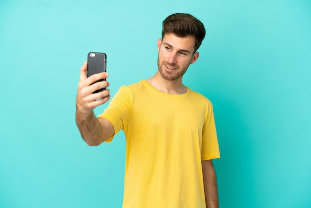 Jeune bel homme caucasien isolé sur fond bleu faisant un selfie