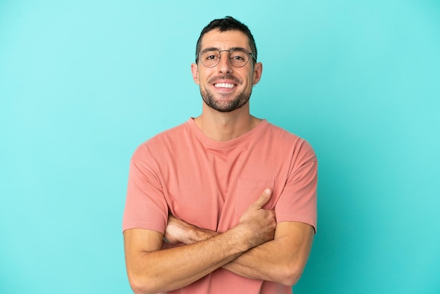 Jeune bel homme caucasien isolé sur fond bleu avec des lunettes avec une expression heureuse