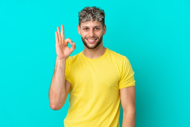 Jeune bel homme caucasien isolé sur fond bleu montrant un signe ok avec les doigts