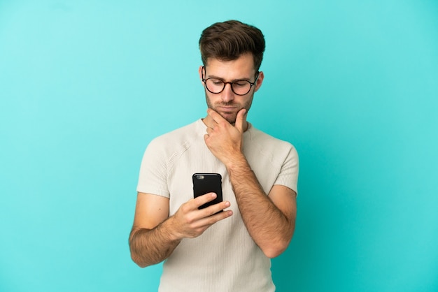 Jeune bel homme caucasien isolé sur fond bleu pensant et envoyant un message