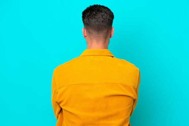 Jeune bel homme caucasien isolé sur fond bleu en position arrière