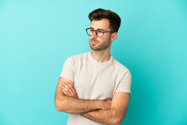 Jeune bel homme caucasien isolé sur fond bleu regardant sur le côté