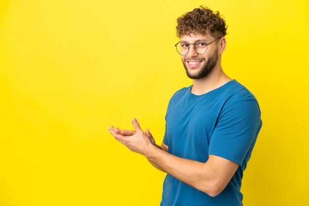 Jeune bel homme caucasien isolé sur fond jaune applaudissant