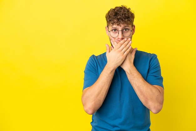 Jeune bel homme caucasien isolé sur fond jaune couvrant la bouche avec les mains