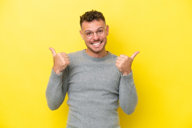 Jeune bel homme caucasien isolé sur fond jaune avec le geste du pouce levé et souriant