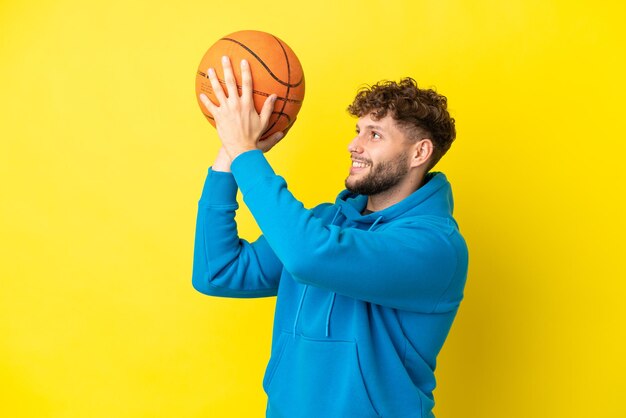 Jeune bel homme caucasien isolé sur fond jaune jouant au basket