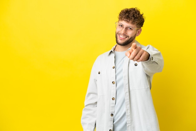 Jeune bel homme caucasien isolé sur fond jaune pointant vers l'avant avec une expression heureuse