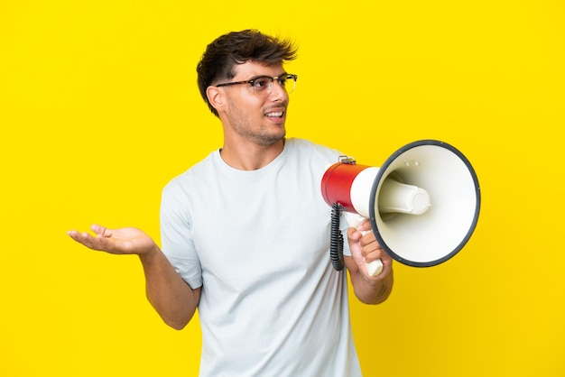 Jeune bel homme caucasien isolé sur fond jaune tenant un mégaphone et avec une expression faciale surprise