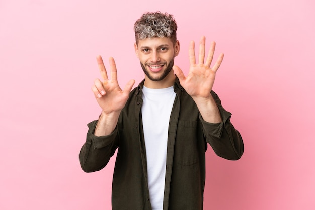 Jeune bel homme caucasien isolé sur fond rose comptant huit avec les doigts