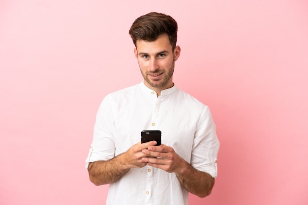 Jeune bel homme caucasien isolé sur fond rose envoyant un message avec le mobile