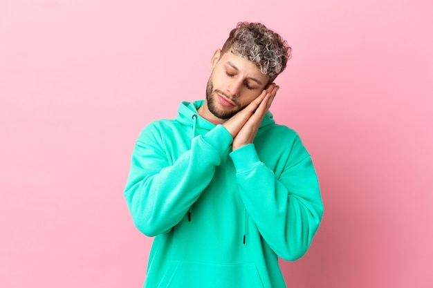 Jeune bel homme caucasien isolé sur fond rose faisant un geste de sommeil dans une expression adorable