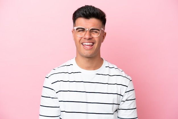 Jeune bel homme caucasien isolé sur fond rose avec des lunettes et une expression heureuse