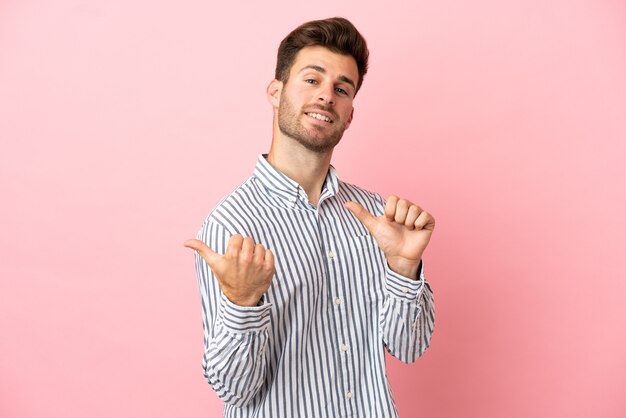 Jeune bel homme caucasien isolé sur fond rose pointant vers le côté pour présenter un produit